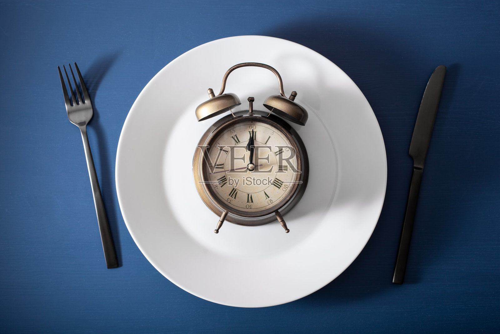 间歇性禁食的概念，生酮饮食，减肥。刀叉，盘子上的闹钟照片摄影图片
