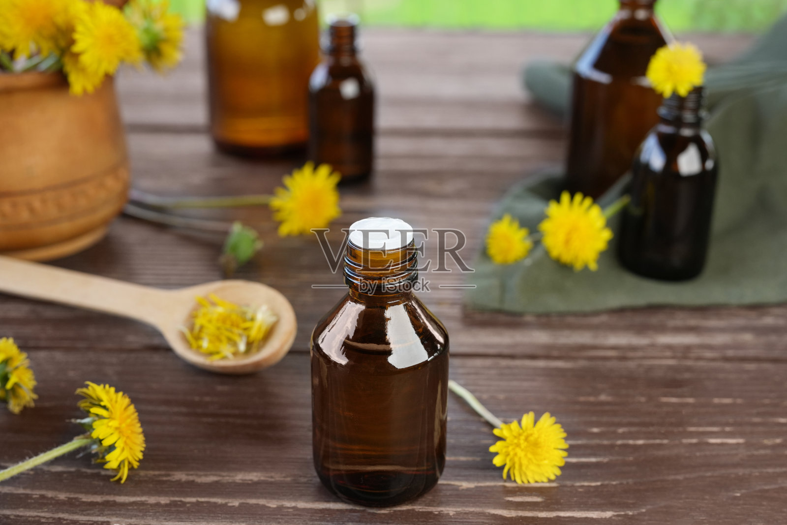 木桌上放着一瓶新鲜的蒲公英花和精油。花精油。绿色医学、顺势疗法、头发皮肤保健、排毒治疗理念。侧视图。照片摄影图片