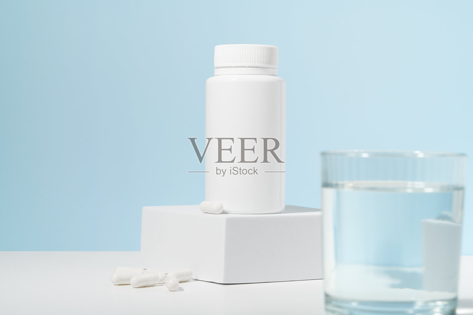 底座上放着一罐药片的白色模型，蓝色背景上放着一杯水。药学、医药、保健和膳食补充剂的概念。照片摄影图片