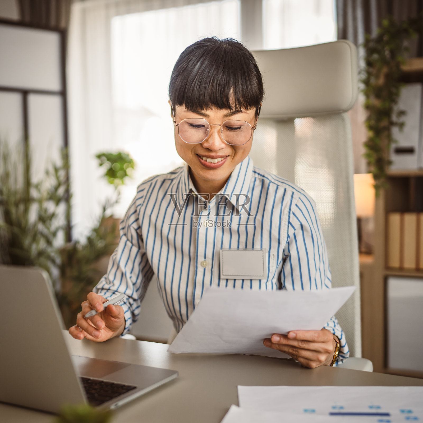戴着眼镜的成熟的日本女人坐在办公室里阅读文件照片摄影图片