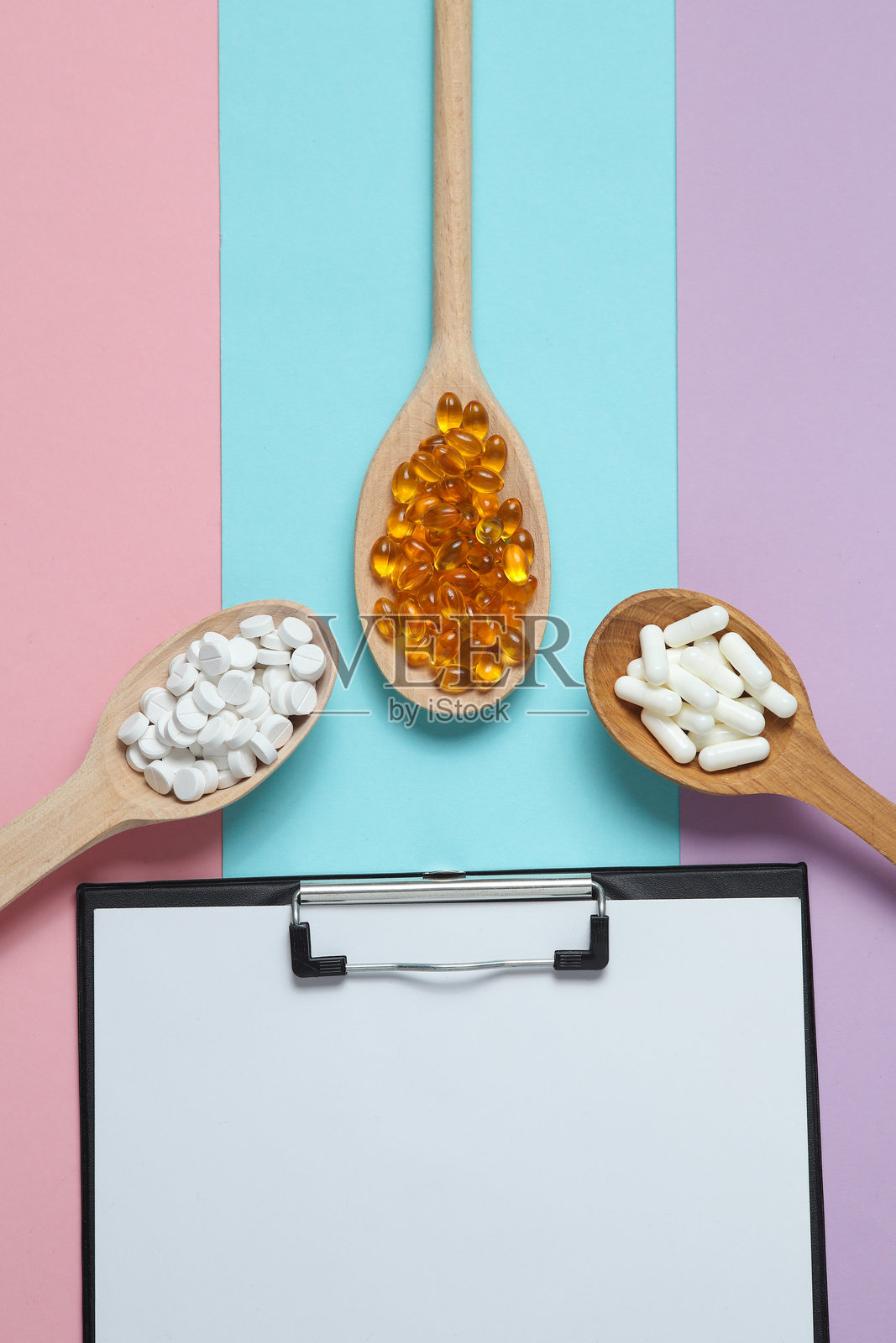 装在木勺里的药片和彩色背景上的剪贴板照片摄影图片