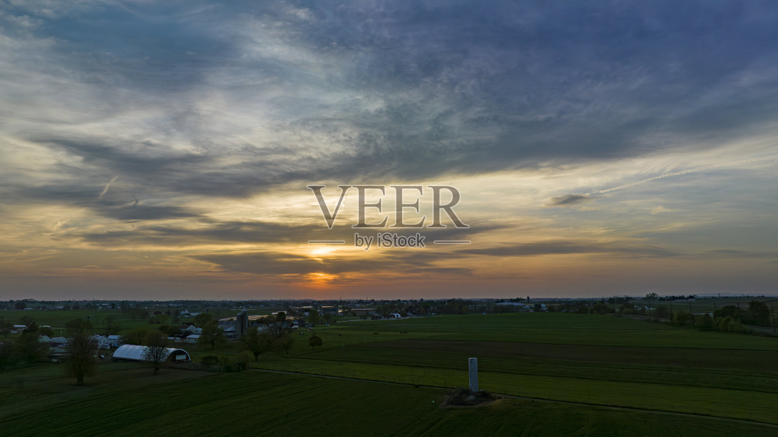 戏剧性的日落投下温暖的光芒在乡村景观与剪影的树木和建筑物照片摄影图片