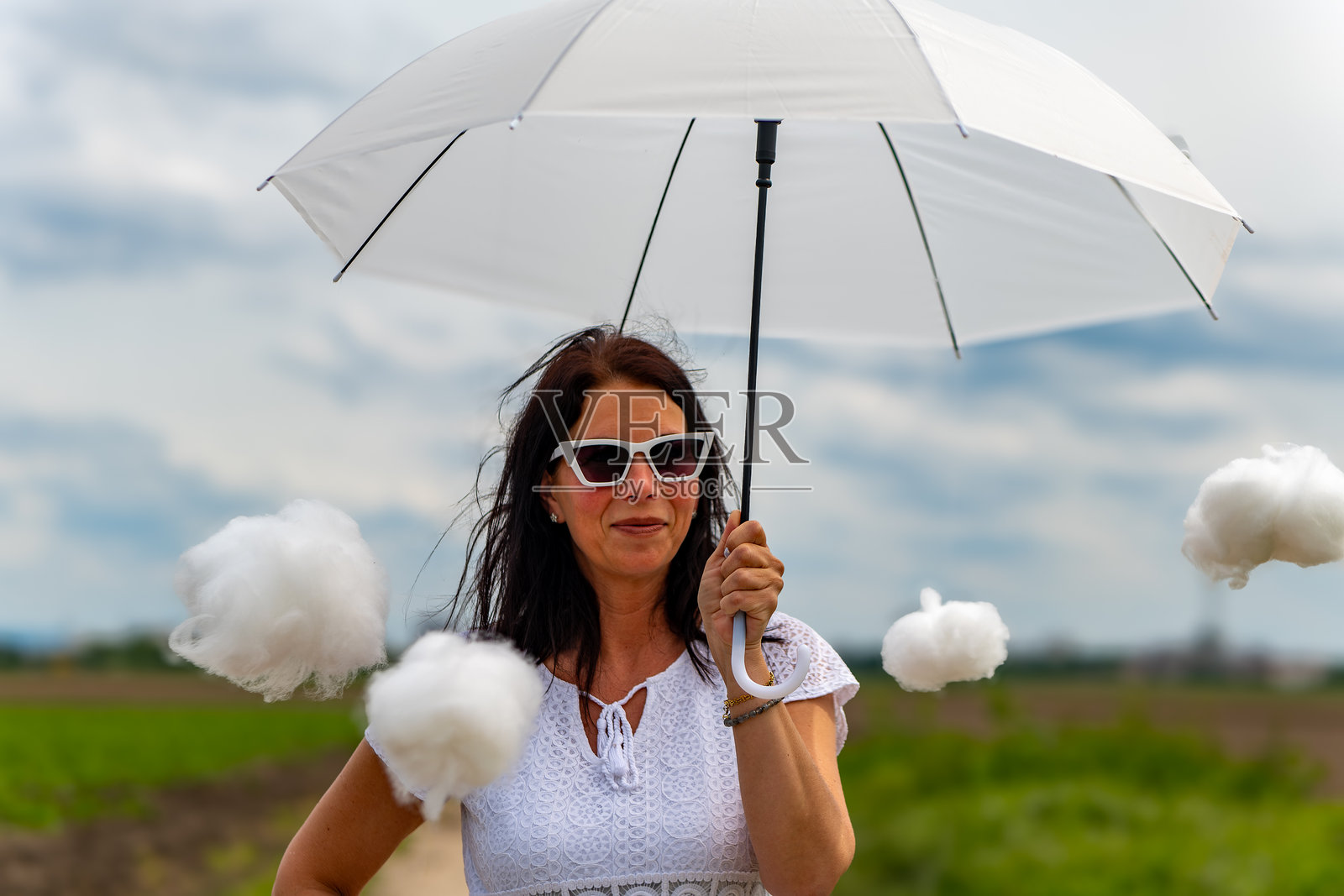 一个女人打着一把白色的伞，被棉花云包围着照片摄影图片
