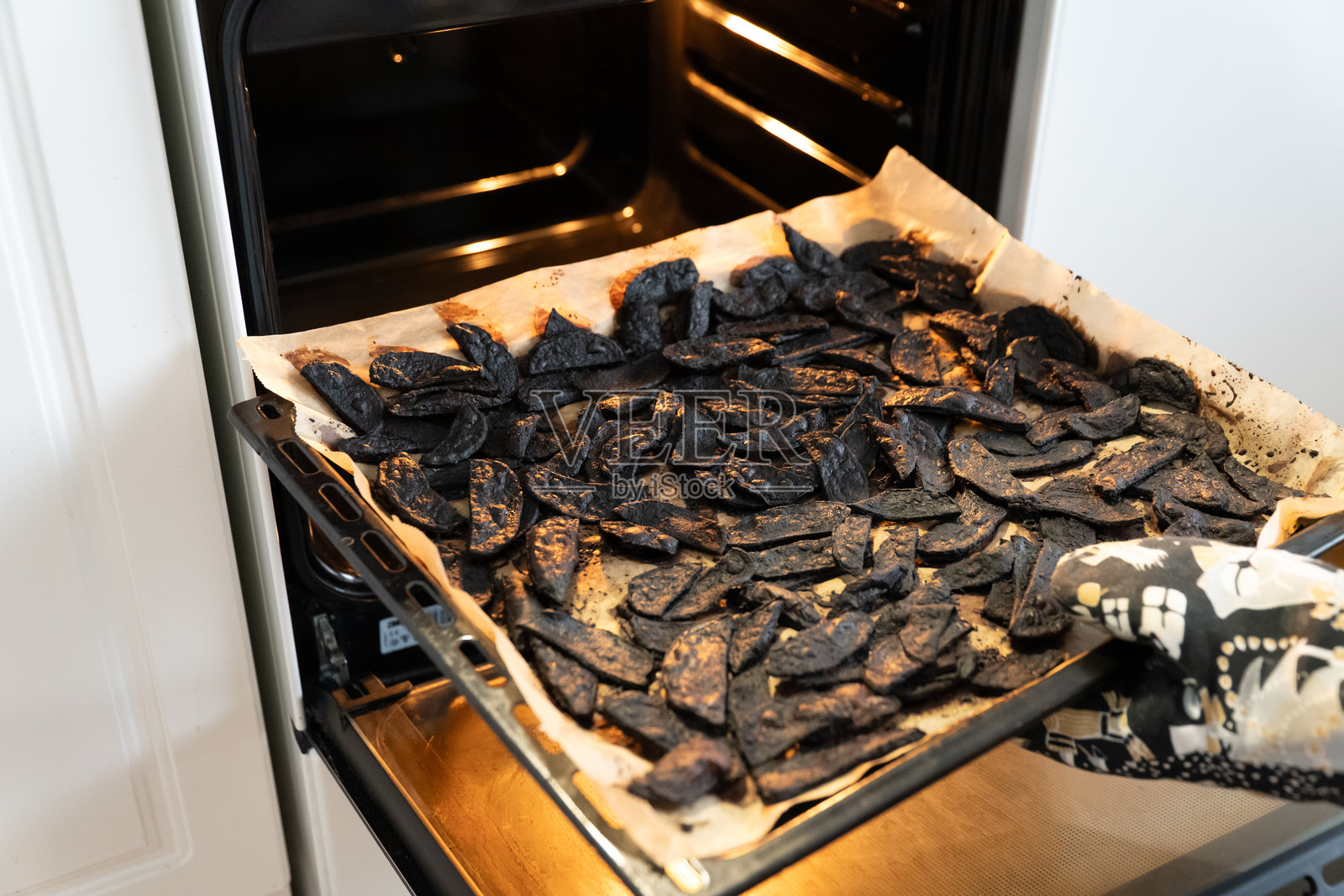 男人从烤箱中取出烧焦的土豆。照片摄影图片