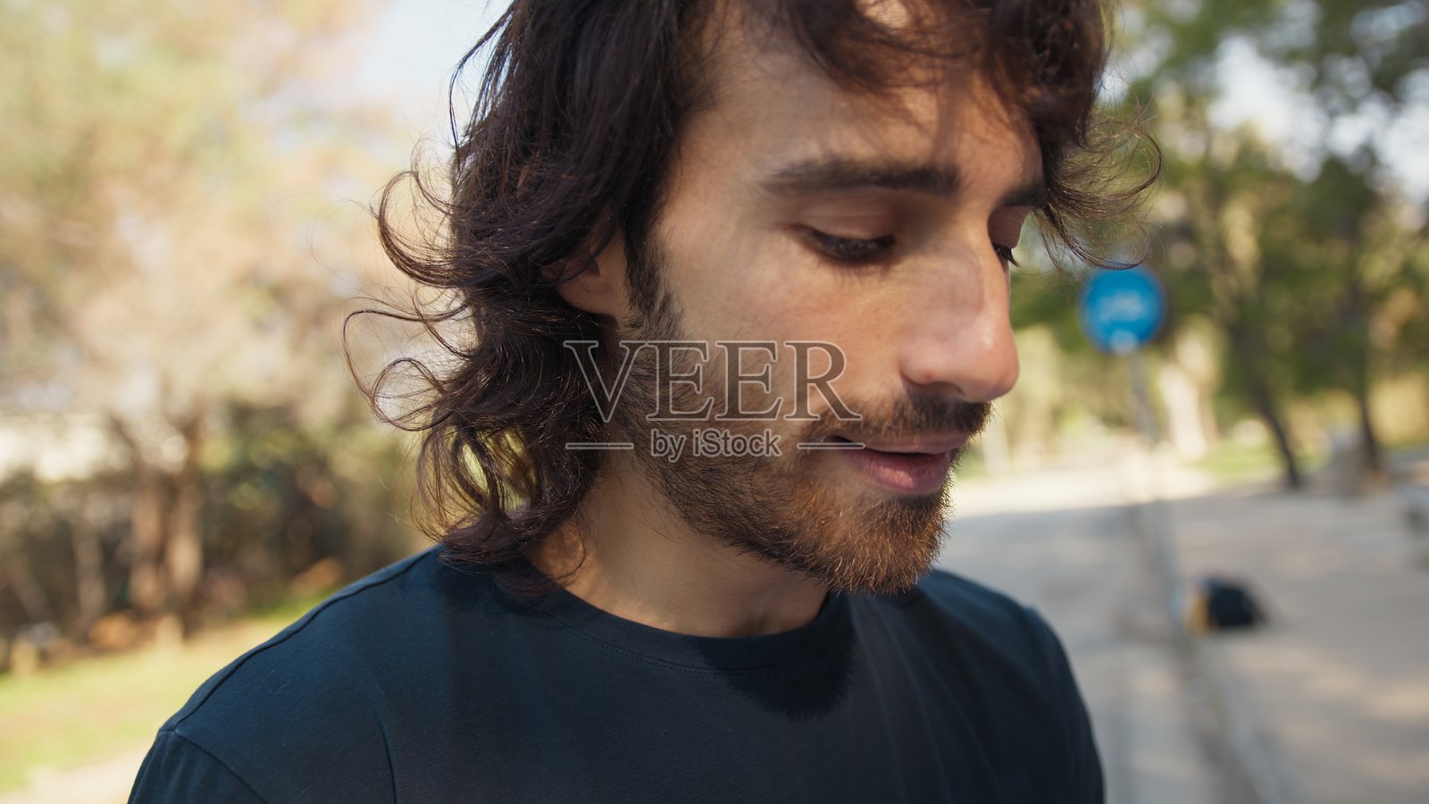 年轻的长发男子在户外公园里阅读一本书，神情忧伤。照片摄影图片