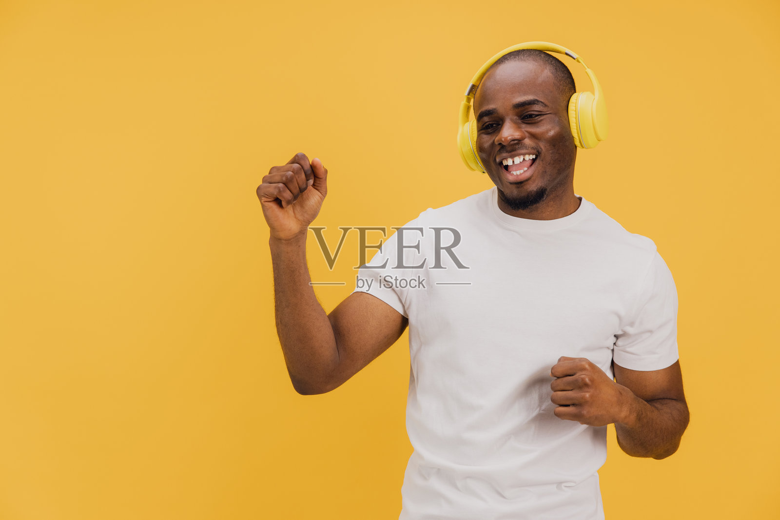 年轻男子戴着黄色耳机在黄色背景下听音乐并跳舞照片摄影图片