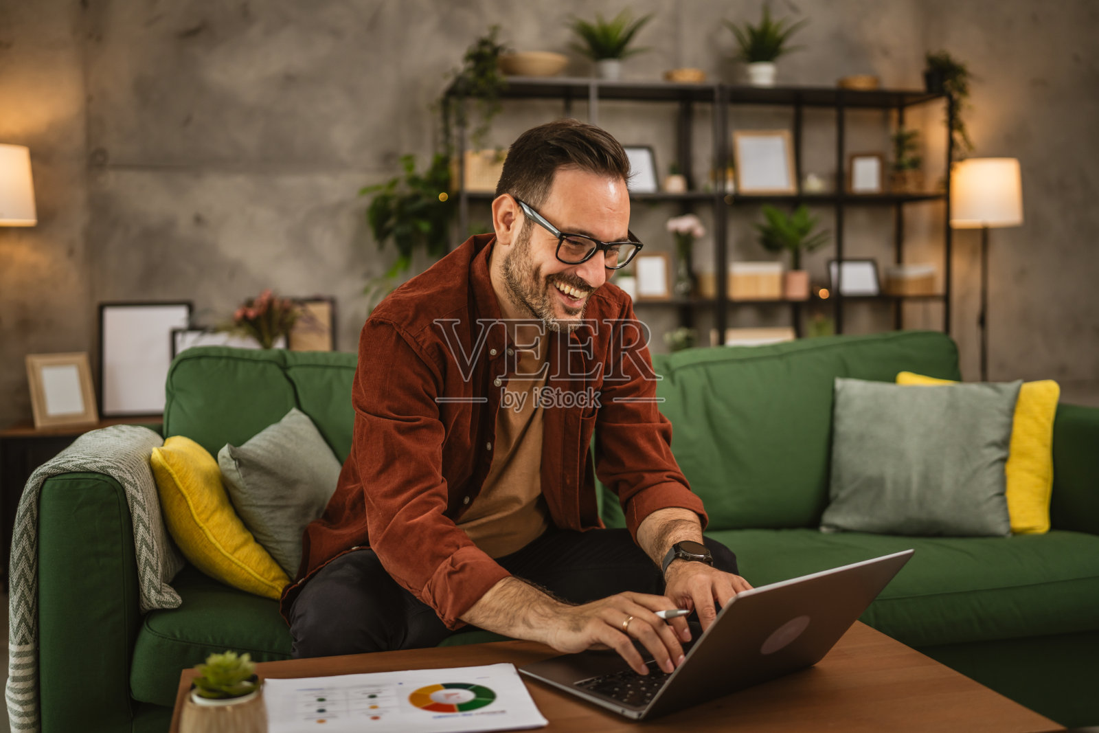 成年快乐的白人男人坐在沙发上，在家里用笔记本电脑工作照片摄影图片