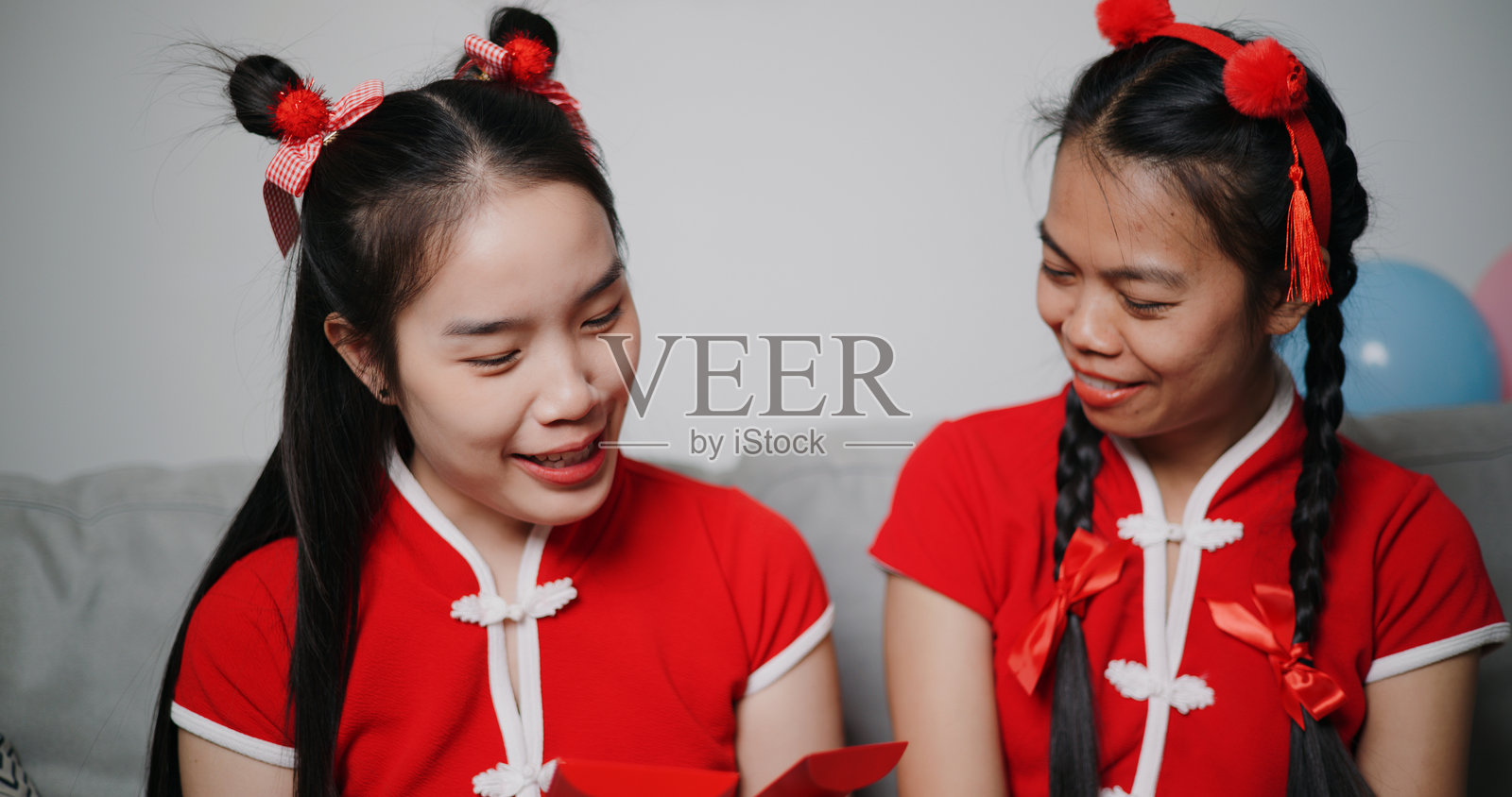 两位穿着传统红色衬衫的亚洲女性坐在家中的沙发上，愉快地交谈并分享美好的感受。照片摄影图片