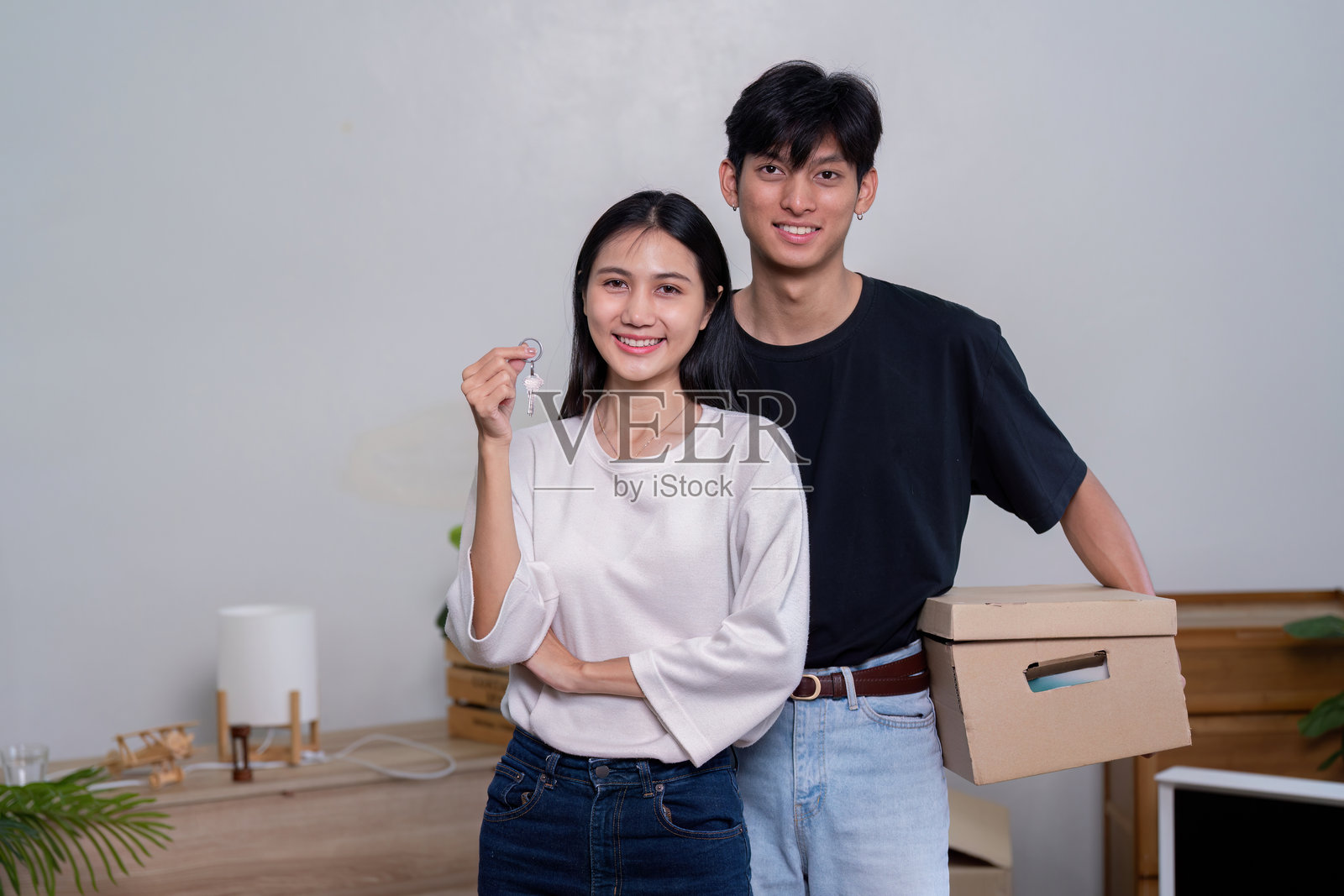 快乐的情侣在新家庆祝，手握钥匙，周围是搬家箱子，空间焕然一新照片摄影图片