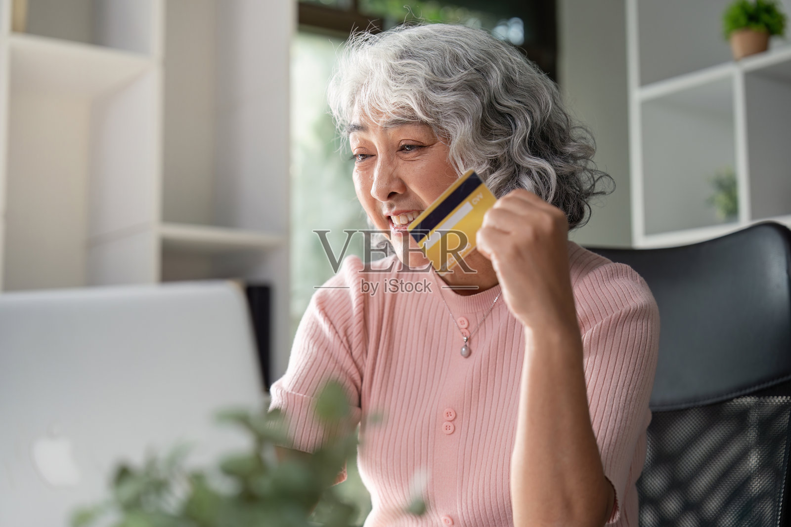 快乐的老年女性在家中庆祝她的网上购物成功，手持信用卡。照片摄影图片