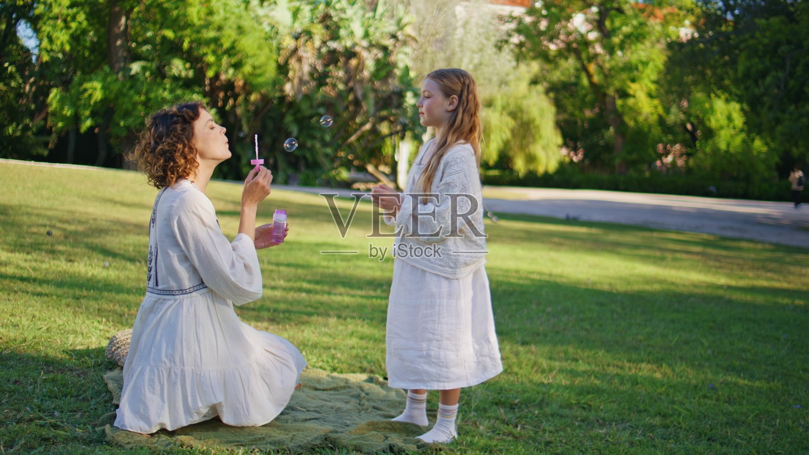 妈妈和孩子在夏季公园的绿草地上一起吹五彩泡泡照片摄影图片