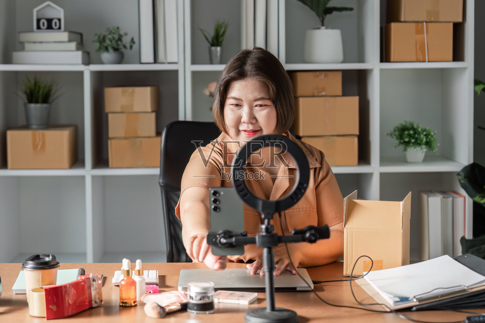 年轻女性热情地进行护肤霜销售直播，展示她整洁的家庭办公室中的产品照片摄影图片