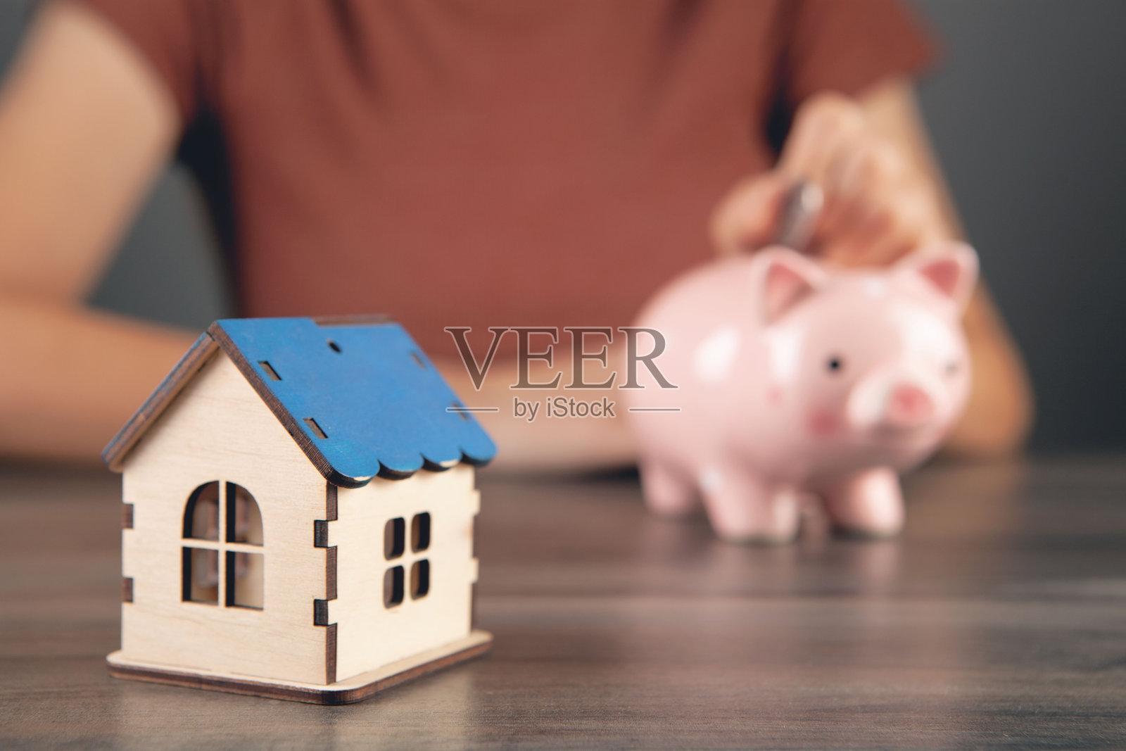 一位女性将硬币放入储蓄罐，旁边是一座房子。照片摄影图片