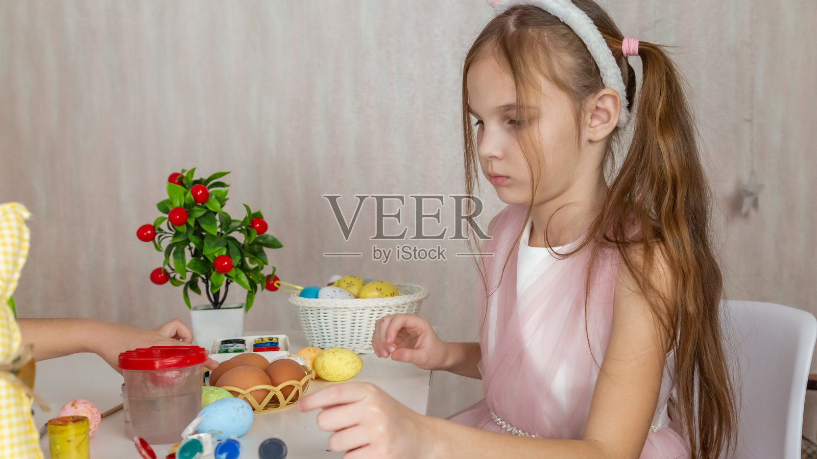 小女孩在绘制彩蛋，为复活节做准备。孩子头戴兔耳朵，手中拿着涂色的复活节彩蛋。照片摄影图片