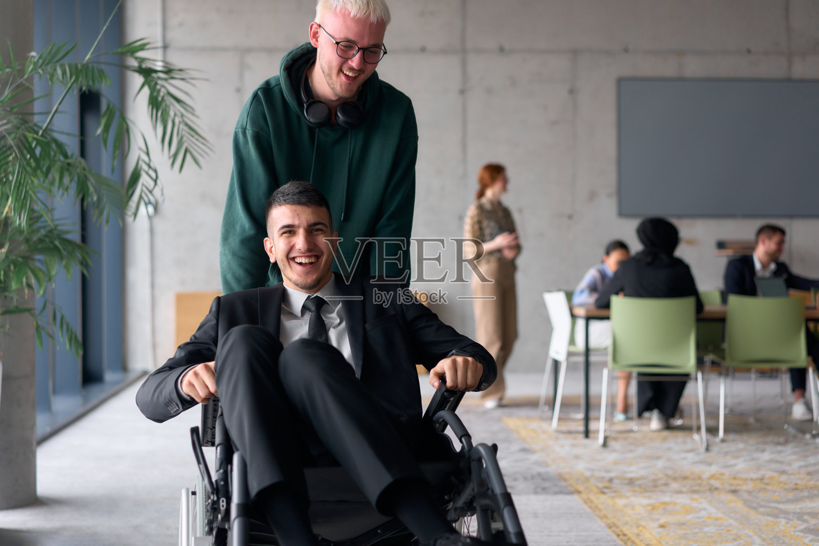 员工在办公室里推着轮椅中的主管，欢声笑语，气氛愉快。照片摄影图片