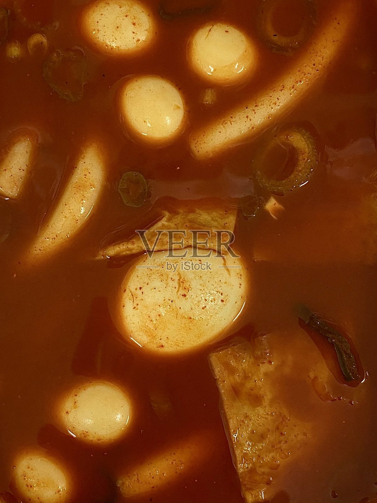 辣味韩国炒年糕，配有嚼劲十足的米糕，浸泡在鲜艳的红色酱汁中，上面撒有芝麻和葱花。这是一种因其令人上瘾的味道和令人满意的口感而广受欢迎的街头小吃。照片摄影图片