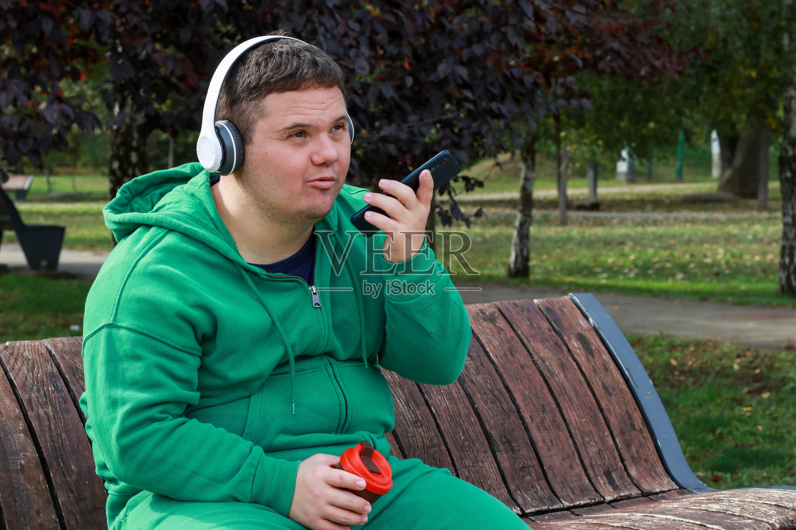 年轻男子在公共公园里悠闲地喝着咖啡，患有唐氏综合症。照片摄影图片