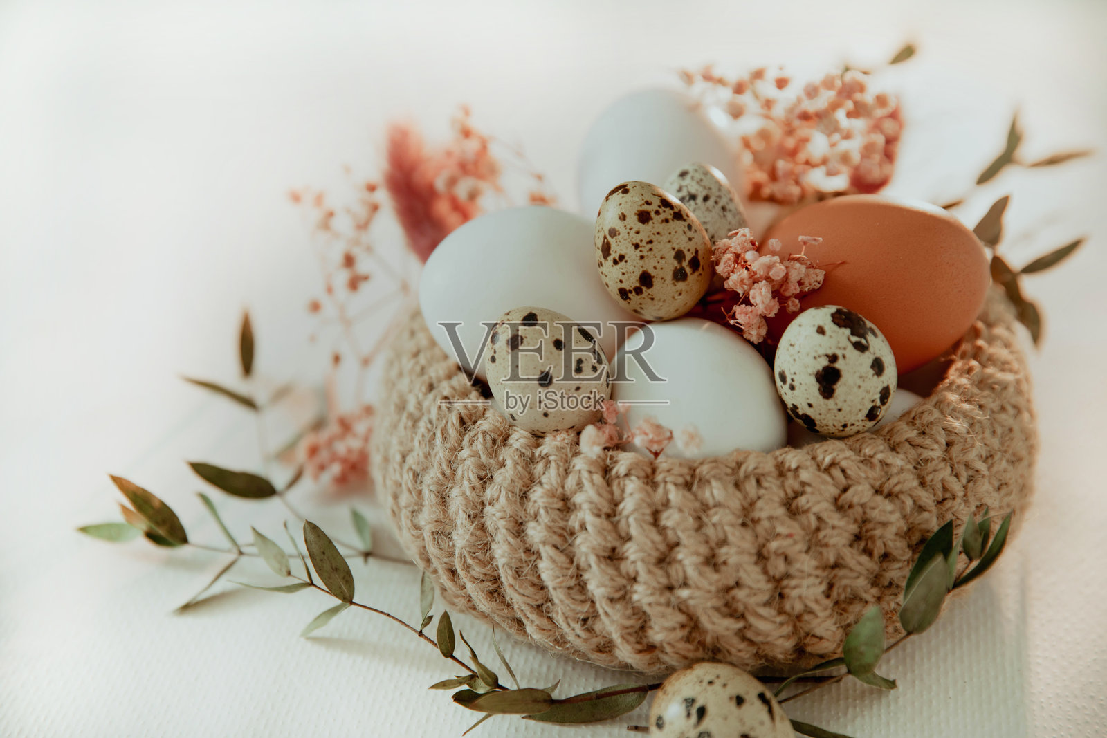 复活节的白色和棕色鸡蛋放在装有花朵的篮子里，背景为白色。照片摄影图片