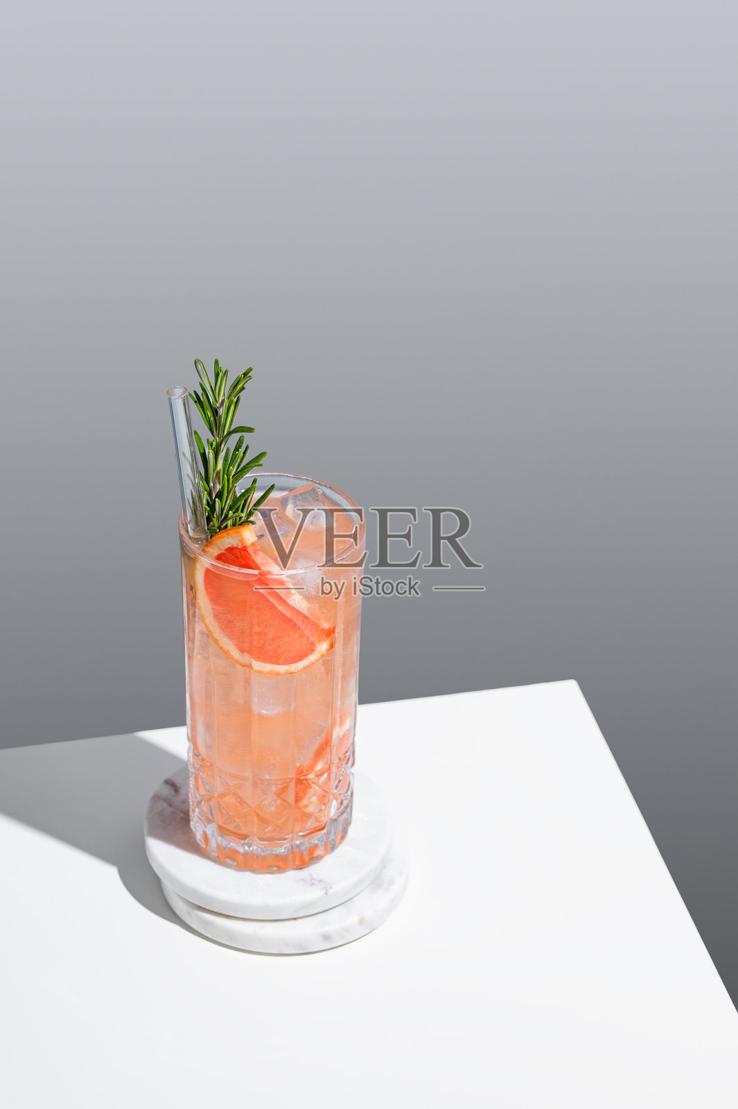 清爽的鸡尾酒，杯中有葡萄柚、迷迭香和冰块，背景为灰色，带有阴影。照片摄影图片