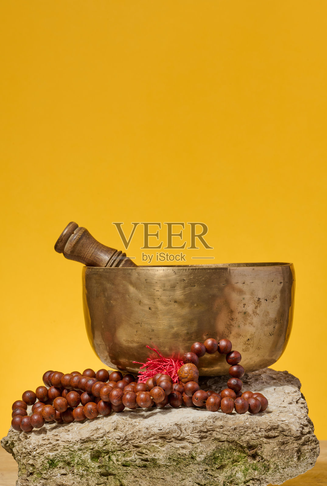 铜制唱碗、木棒和祈祷珠放在石头上，背景为黄色照片摄影图片