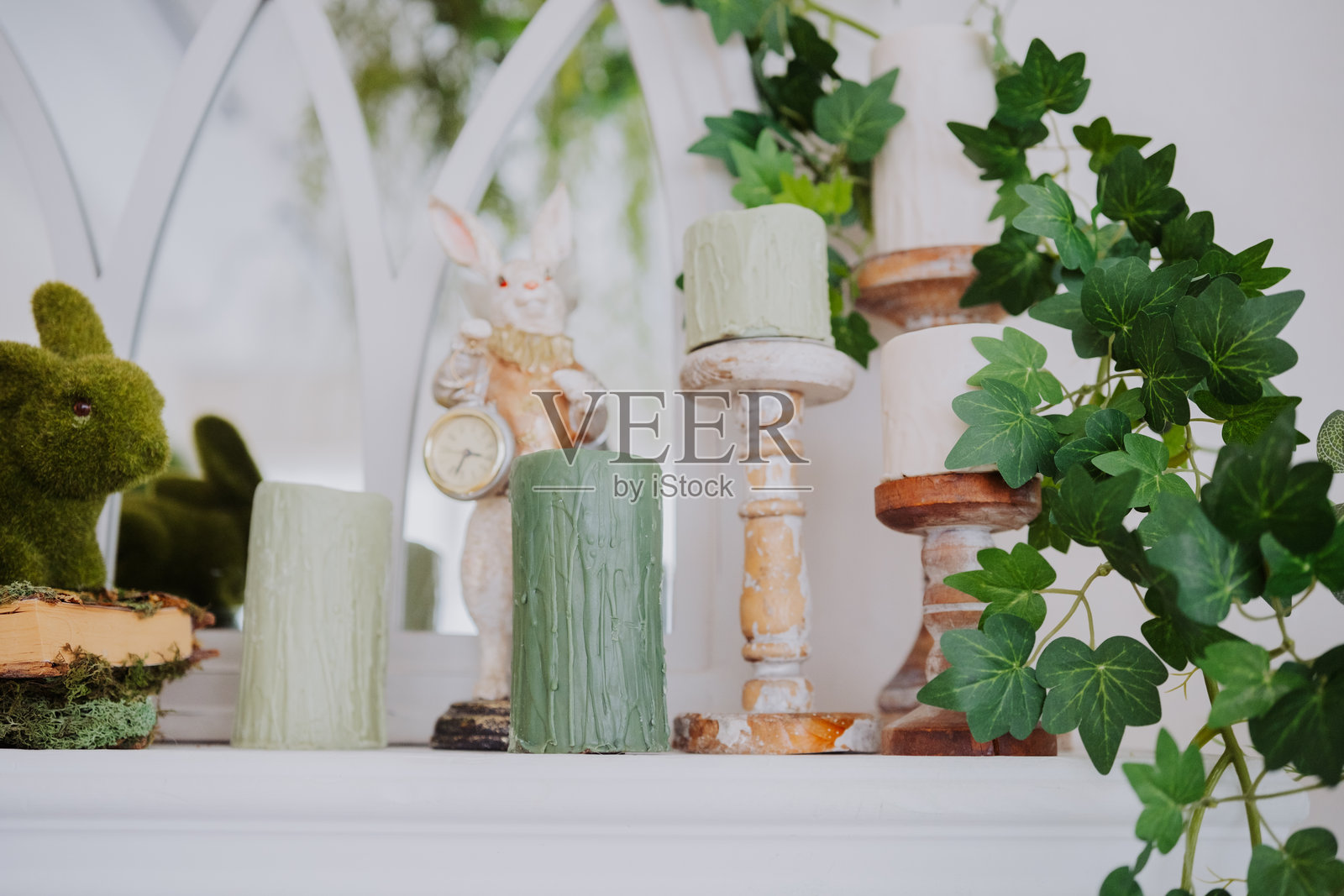 装饰性架子上摆放着蜡烛、绿植和一只兔子雕像，置于明亮的空间中照片摄影图片