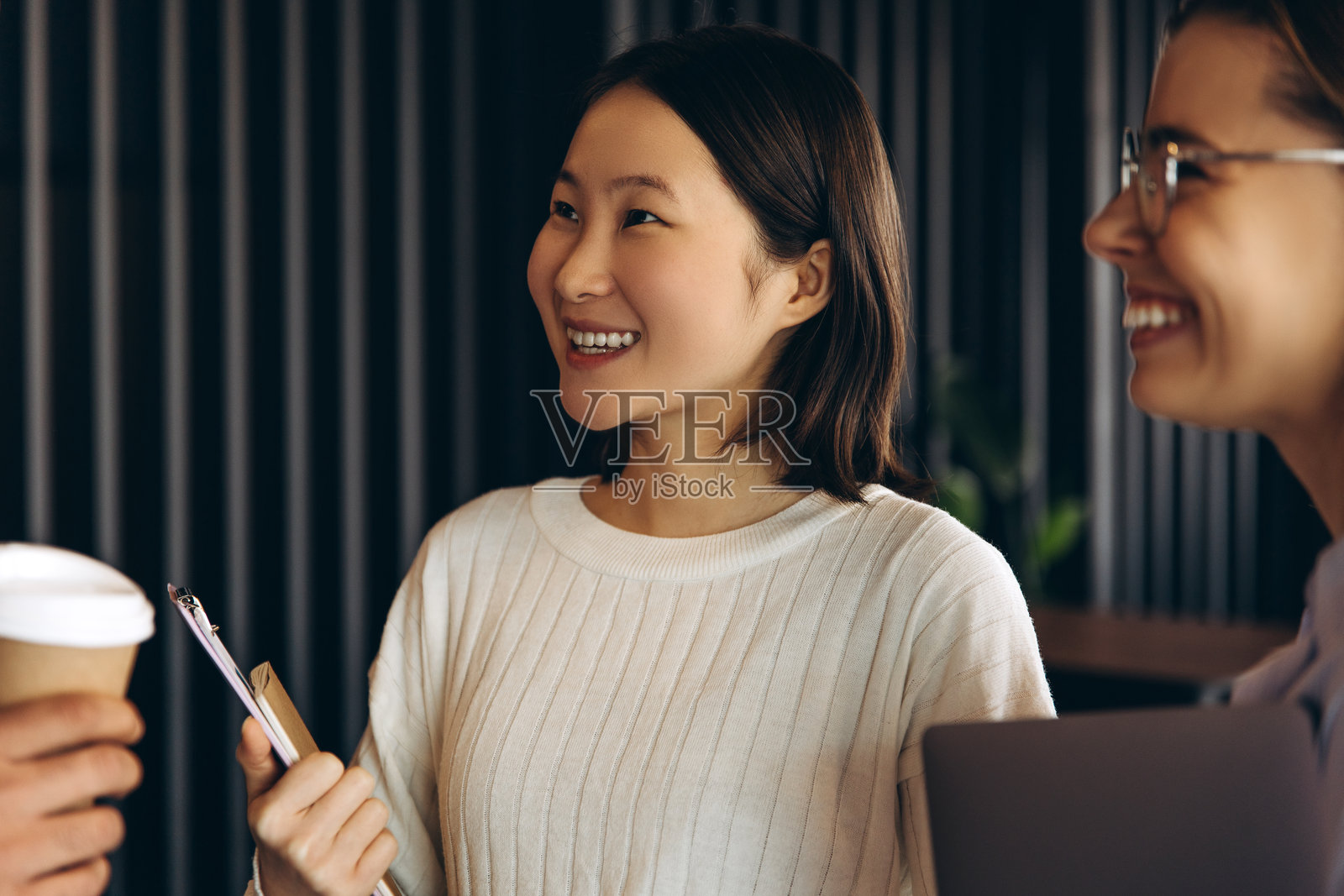 年轻的亚洲女商人手持夹板，微笑着在与同事的非正式会议中。照片摄影图片