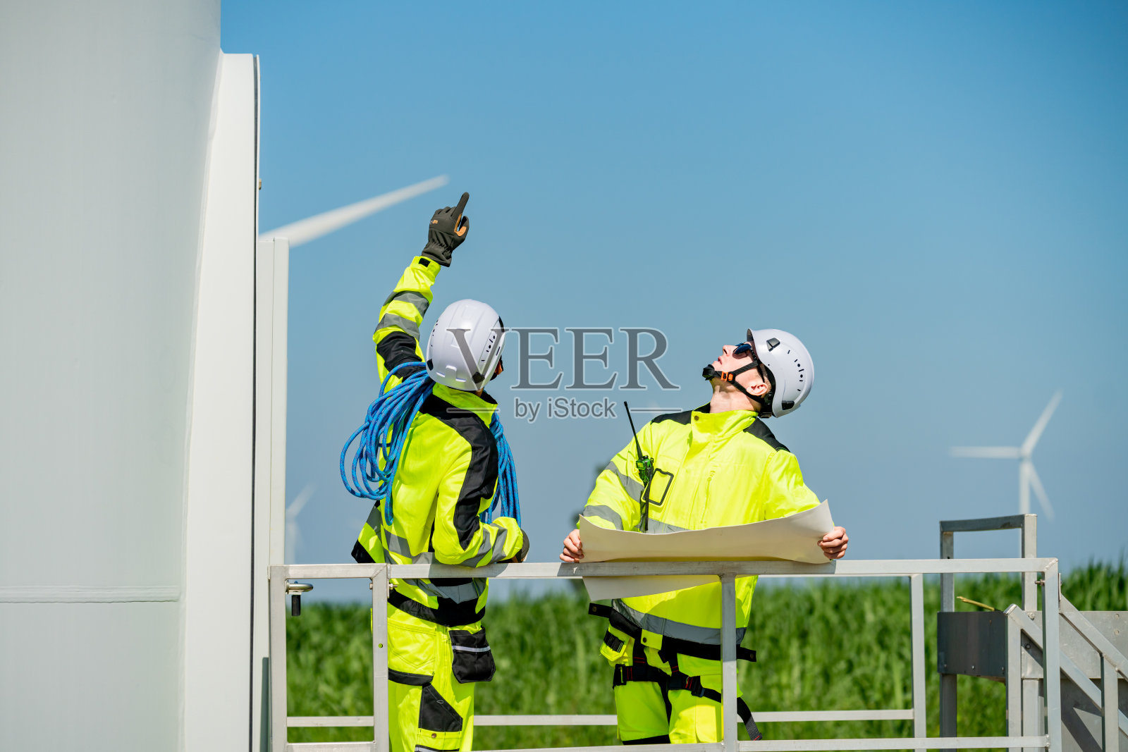 工人在清澈的天空和绿色的风景中检查风力涡轮机的计划，同时讨论安全措施。照片摄影图片