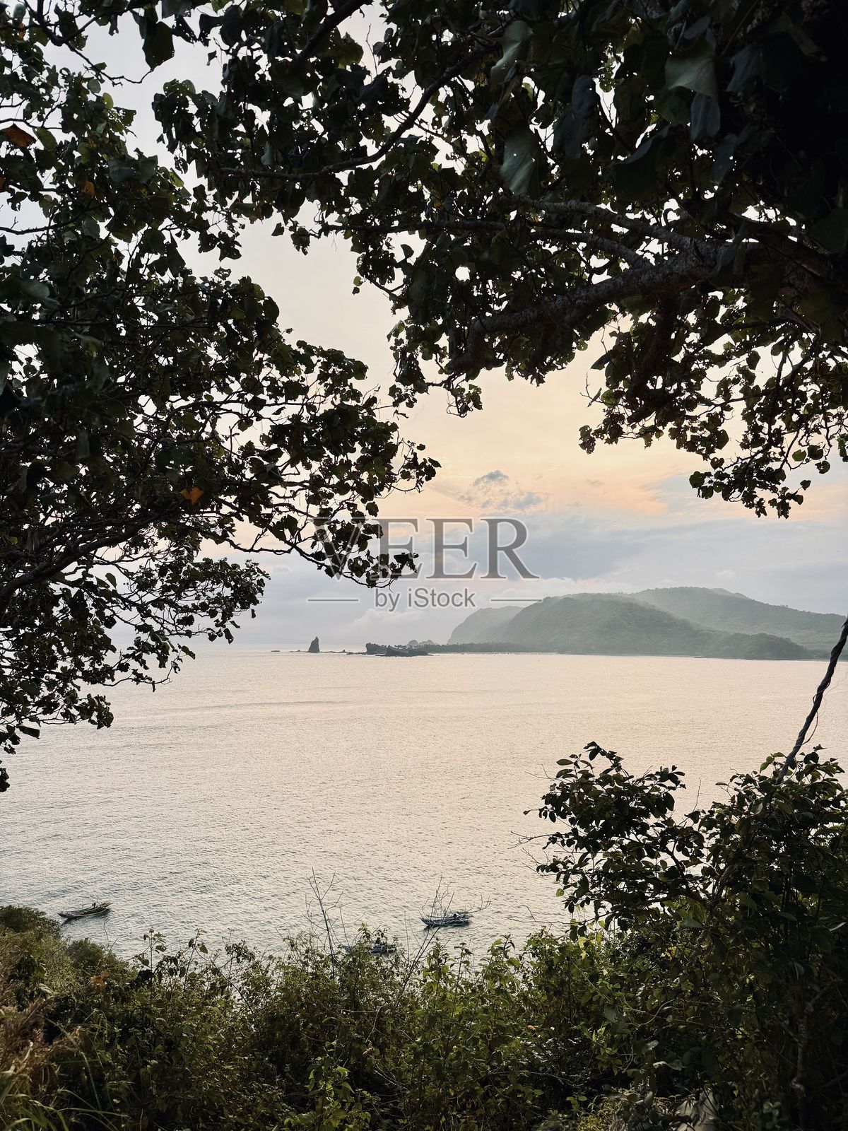 日落时分的印尼杰姆伯帕扬甘海滩美景——被郁郁葱葱的绿植环绕，俯瞰宁静的海洋，传统渔船，海岸风光，热带岛屿，自然旅游胜地。照片摄影图片