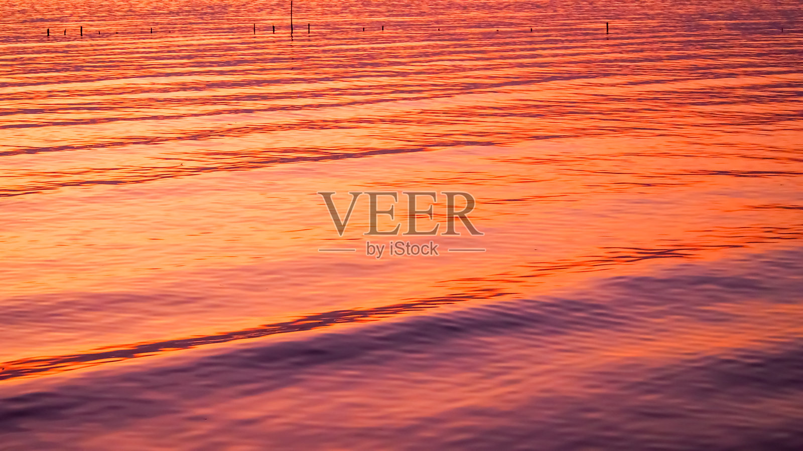 一个宁静的场景，捕捉到温暖金色夕阳下轻柔的水波。平滑的倒影营造出一种宁静而迷人的视觉节奏。照片摄影图片