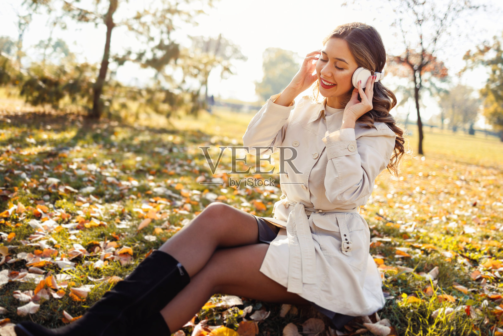 美丽的年轻女性在户外享受无忧无虑的秋日，戴着无线耳机听音乐。照片摄影图片