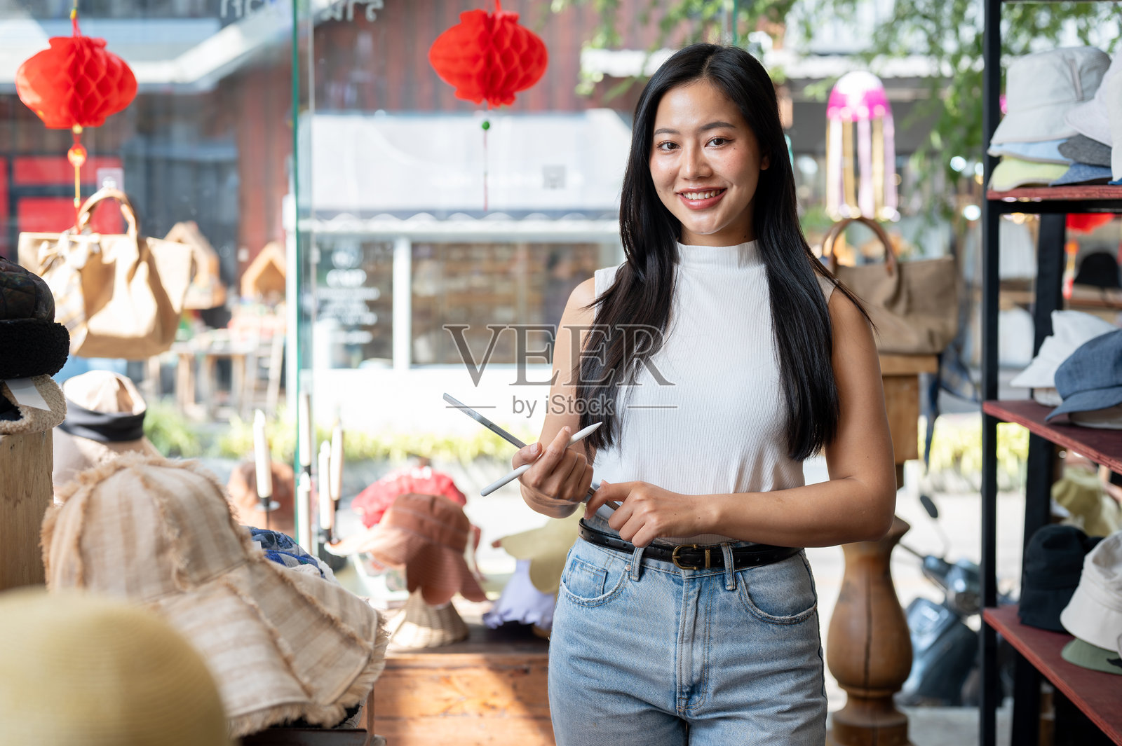 一位自信、美丽的亚洲女性帽子店老板手持平板电脑站在她的店里。照片摄影图片