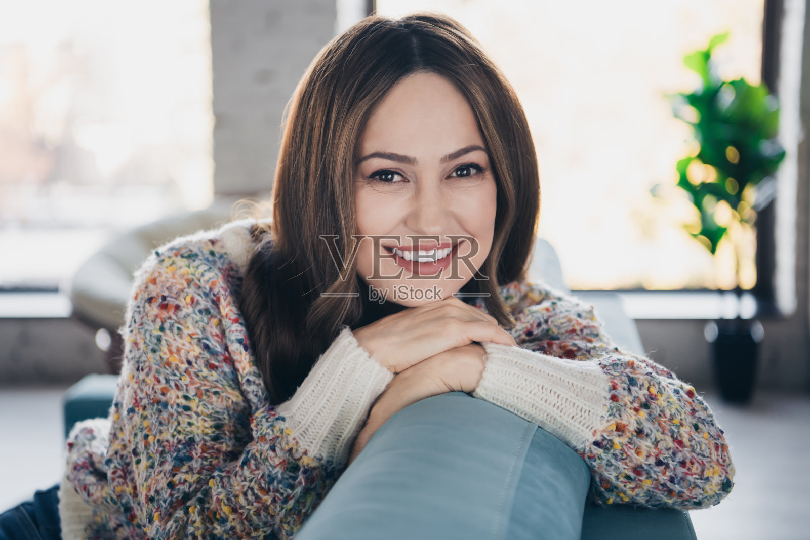 美丽的年轻女性在室内放松，穿着五彩缤纷的毛衣，开心地微笑。照片摄影图片