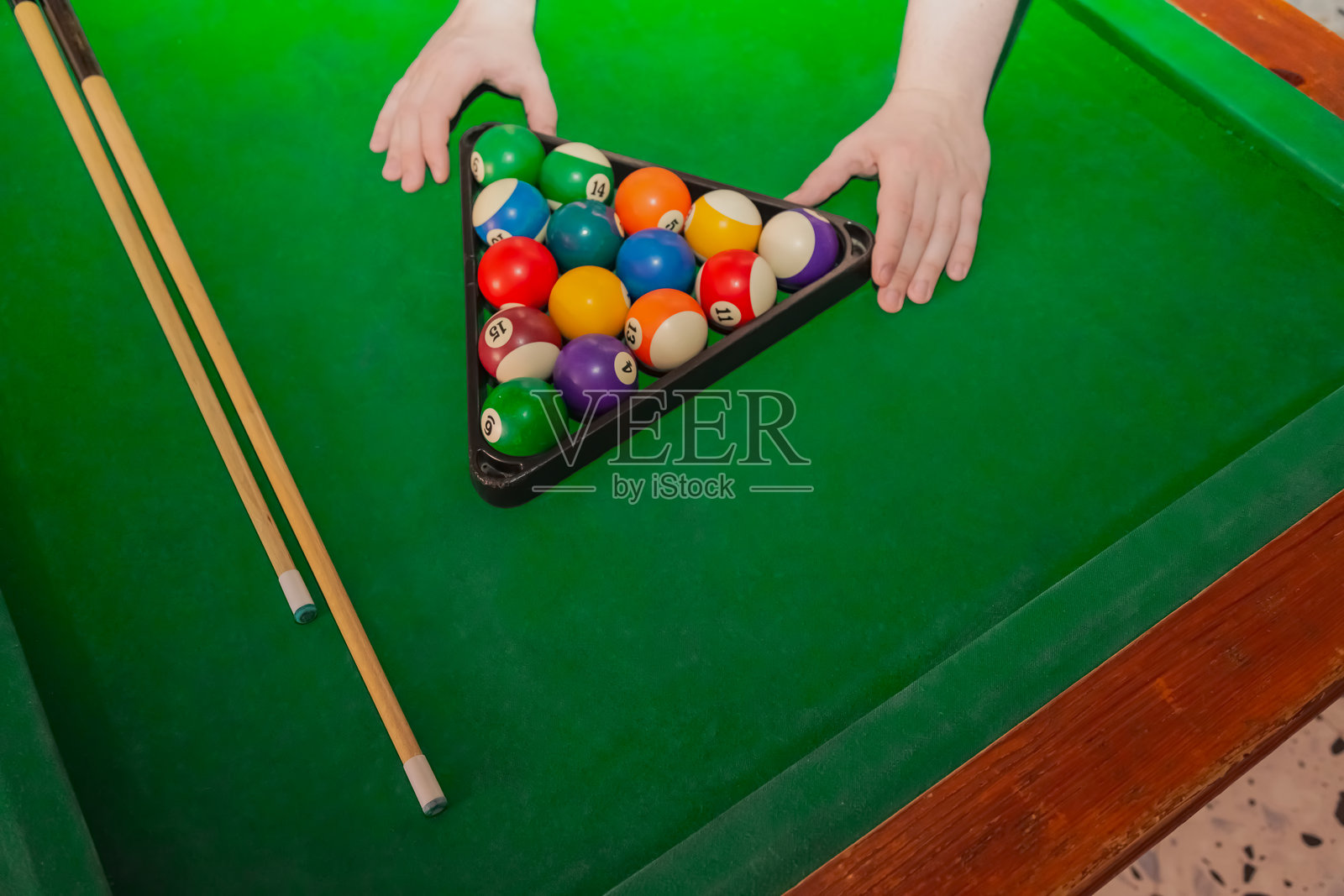 在绿色台布上摆放三角形的台球，初始排列，旁边有两根球杆，绿色台布上的台球金字塔，特写，台球游戏开始。照片摄影图片