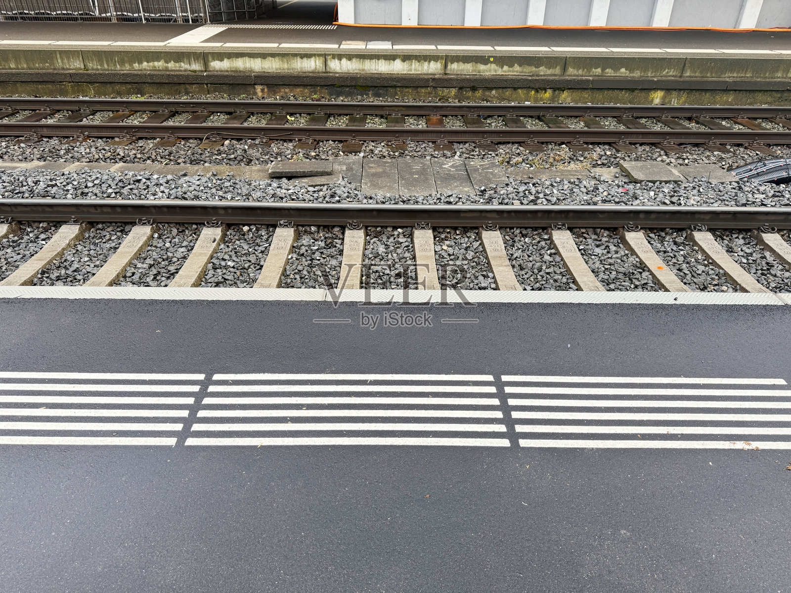 湿润火车站台上的铁路轨道特写，包含碎石、枕木和触觉铺装。照片摄影图片