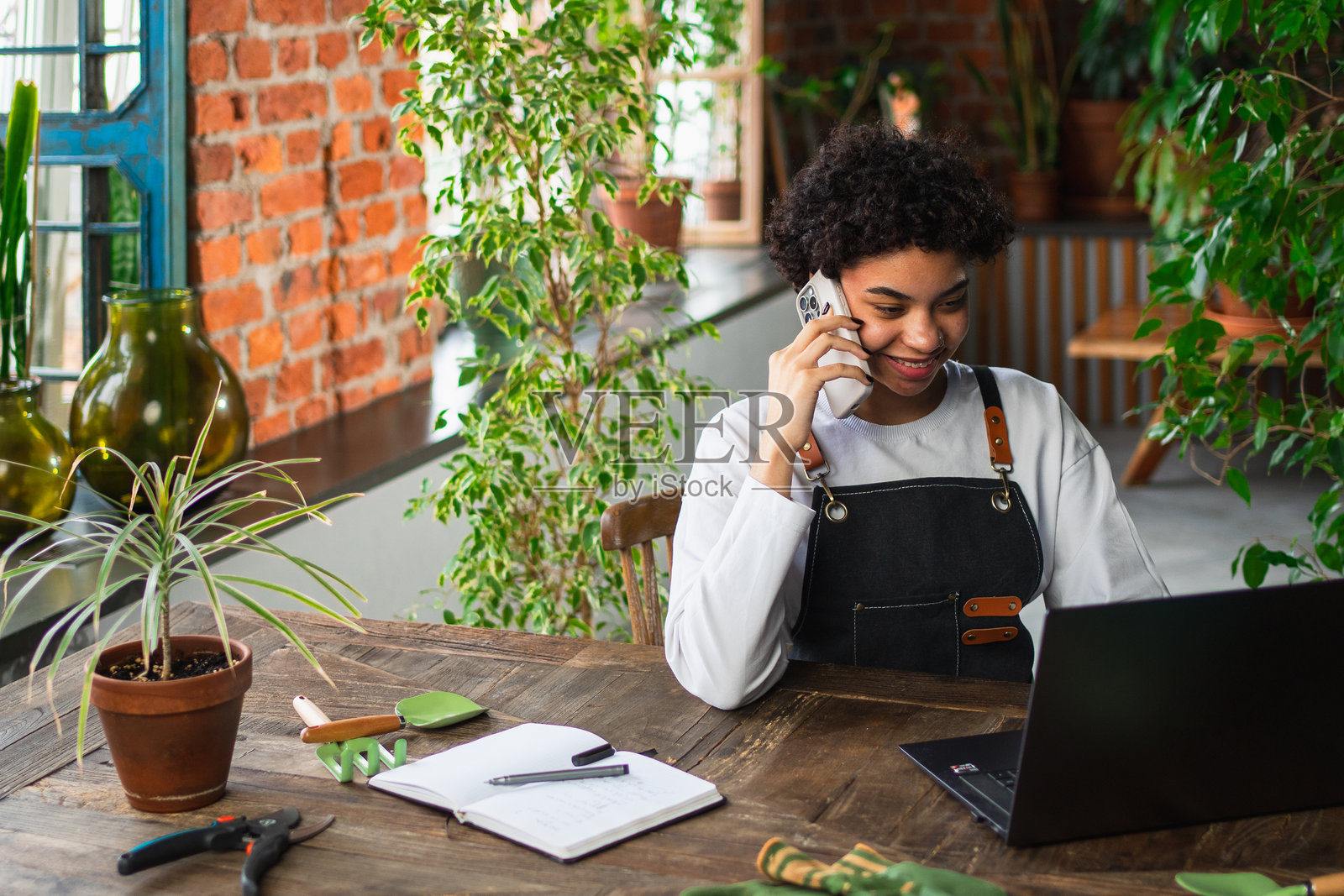 非洲女性花店园丁在植物商店使用笔记本电脑通过电话订购植物，与顾客沟通。女性小企业主在花店工作，经营自己的生意。照片摄影图片