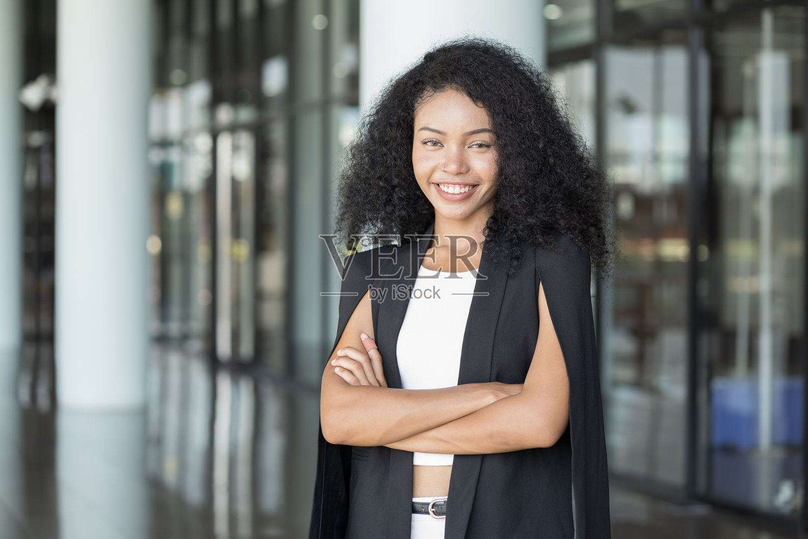 年轻职业女性在办公室工作中双臂交叉的肖像。快乐、自信的年轻职业女性穿着西装，双臂交叉微笑。照片摄影图片