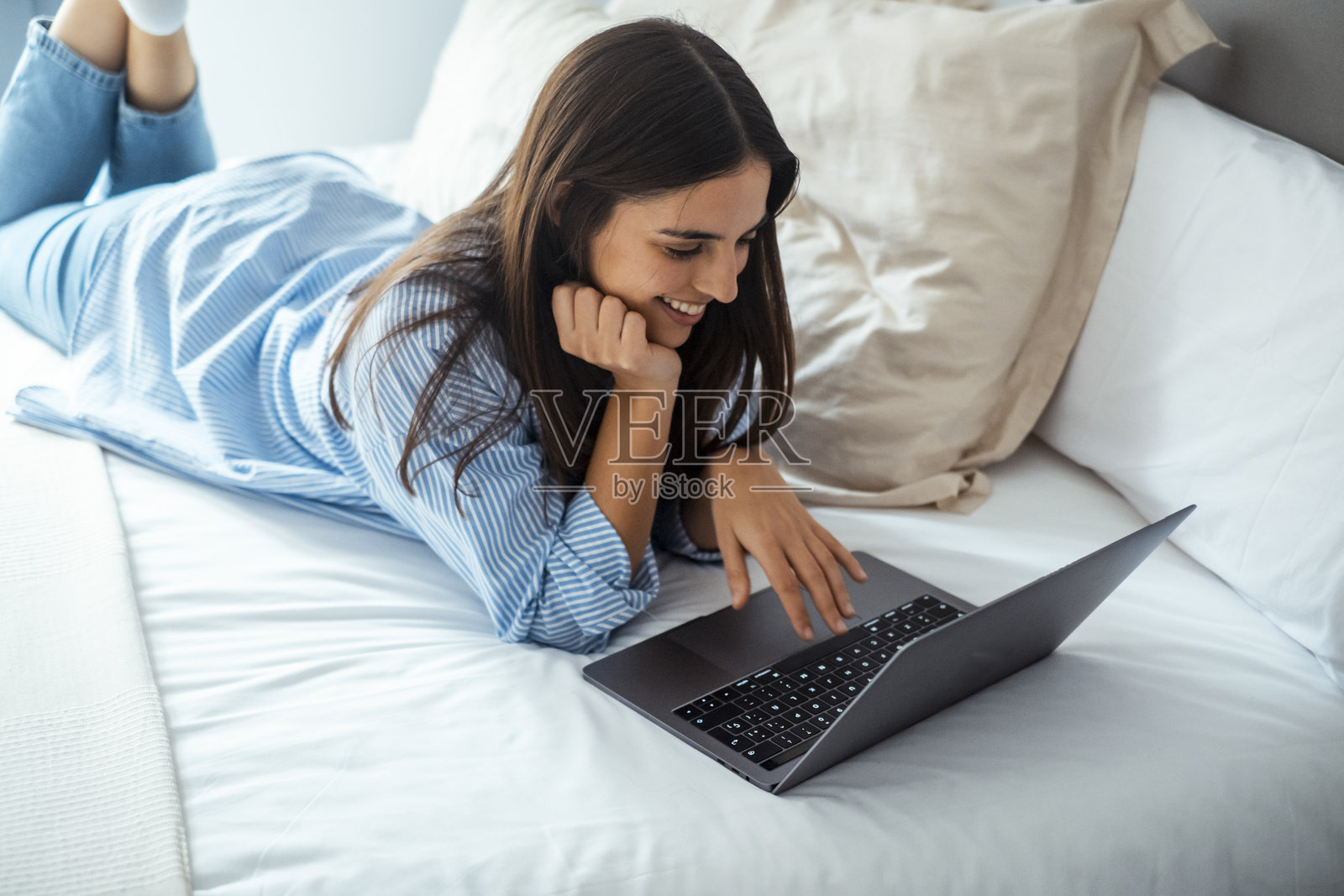 快乐的女孩躺在床上用笔记本电脑发信息，和男朋友聊天或写浪漫信件，微笑的女性与朋友交流，在卧室放松，女性上网浏览。照片摄影图片