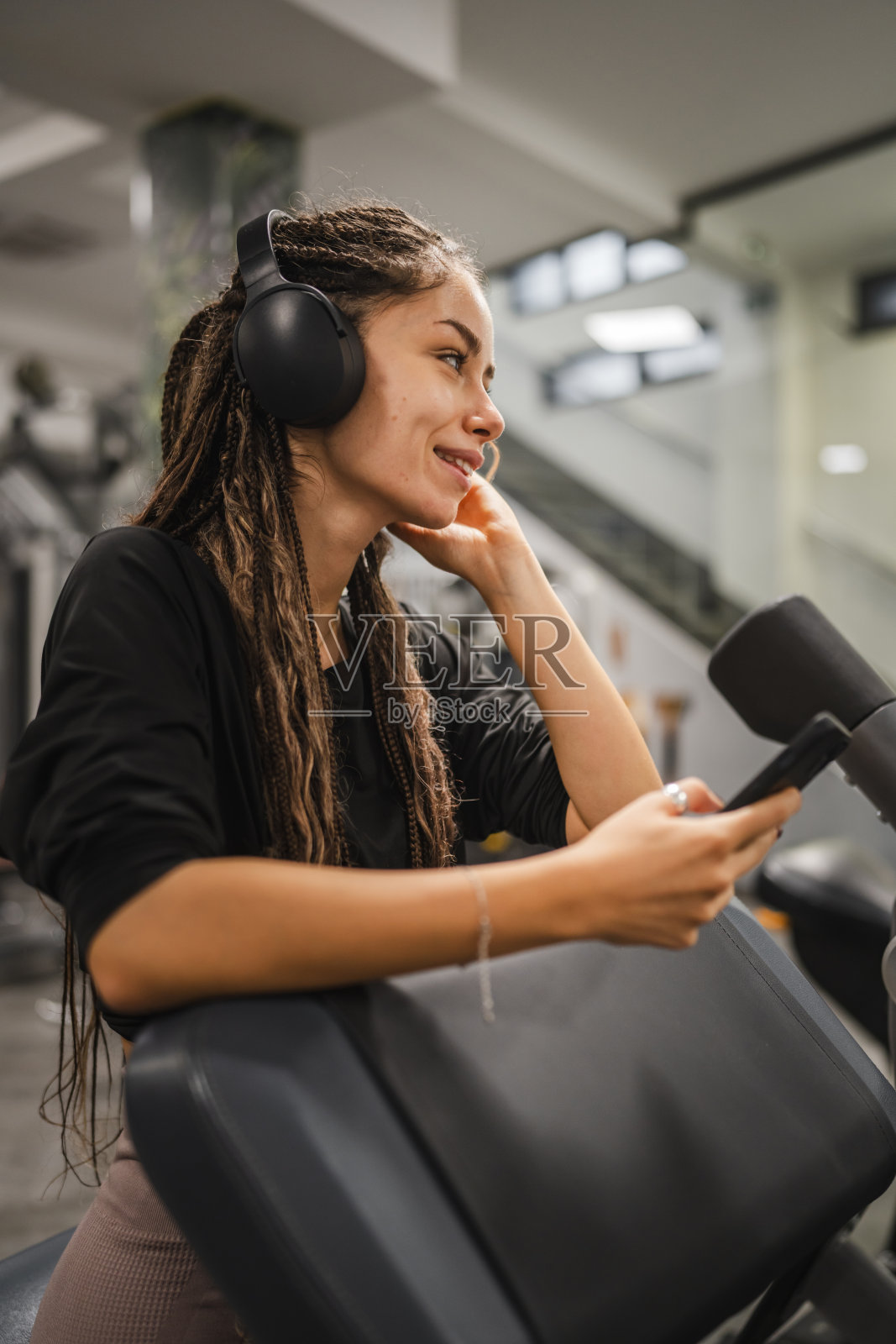 年轻女性戴着耳机在健身房使用手机休息照片摄影图片