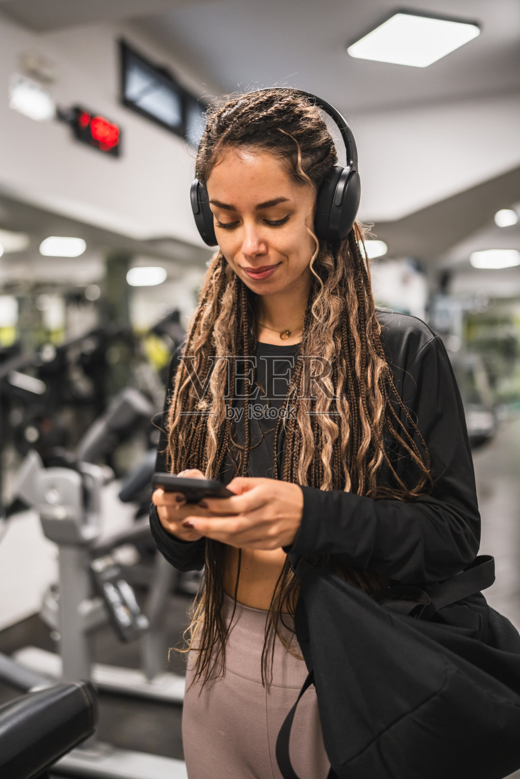 年轻女性戴着耳机，使用手机，训练后回家。照片摄影图片