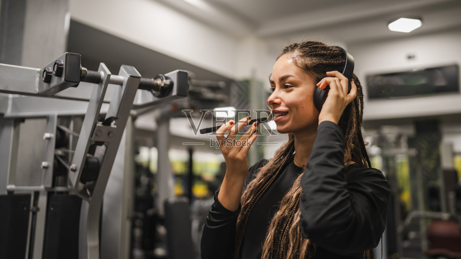 年轻女性戴着耳机在健身房使用手机休息。照片摄影图片