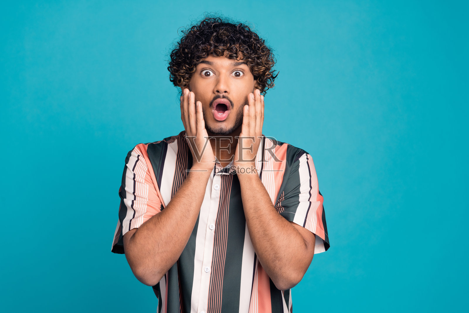 年轻男子张嘴凝视，穿着衬衫，背景为青绿色。照片摄影图片