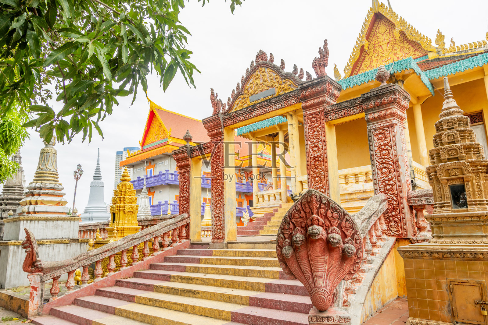 五彩缤纷的黄色佛教猴子寺庙，周围环绕着佛塔和那伽雕像，位于柬埔寨的金边。照片摄影图片