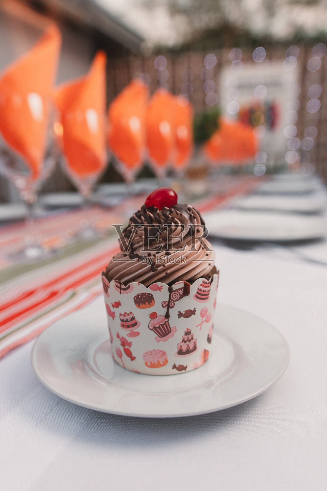 盘子上的巧克力杯子蛋糕上放着一颗樱桃，摆放在一张长桌上。照片摄影图片
