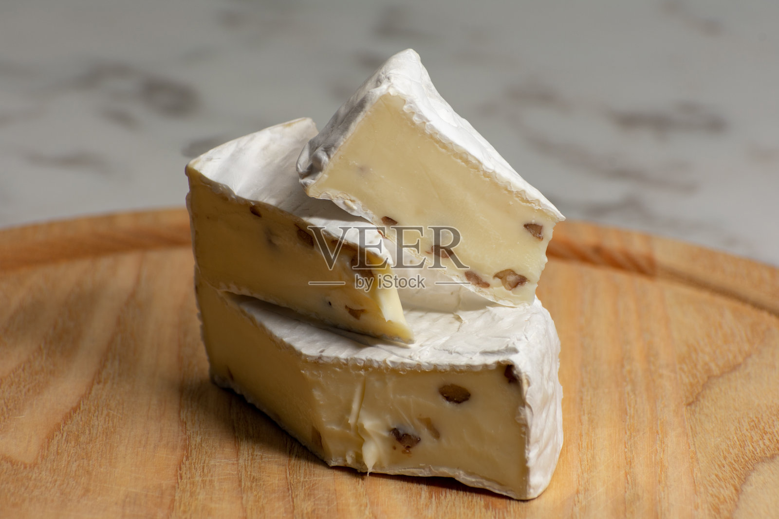 一轮奶油卡门贝尔奶酪，上面撒有坚果，静置在粗犷的木质表面上，背景为纯黑色。丰富的质感和对比形成了优雅的烹饪构图。照片摄影图片