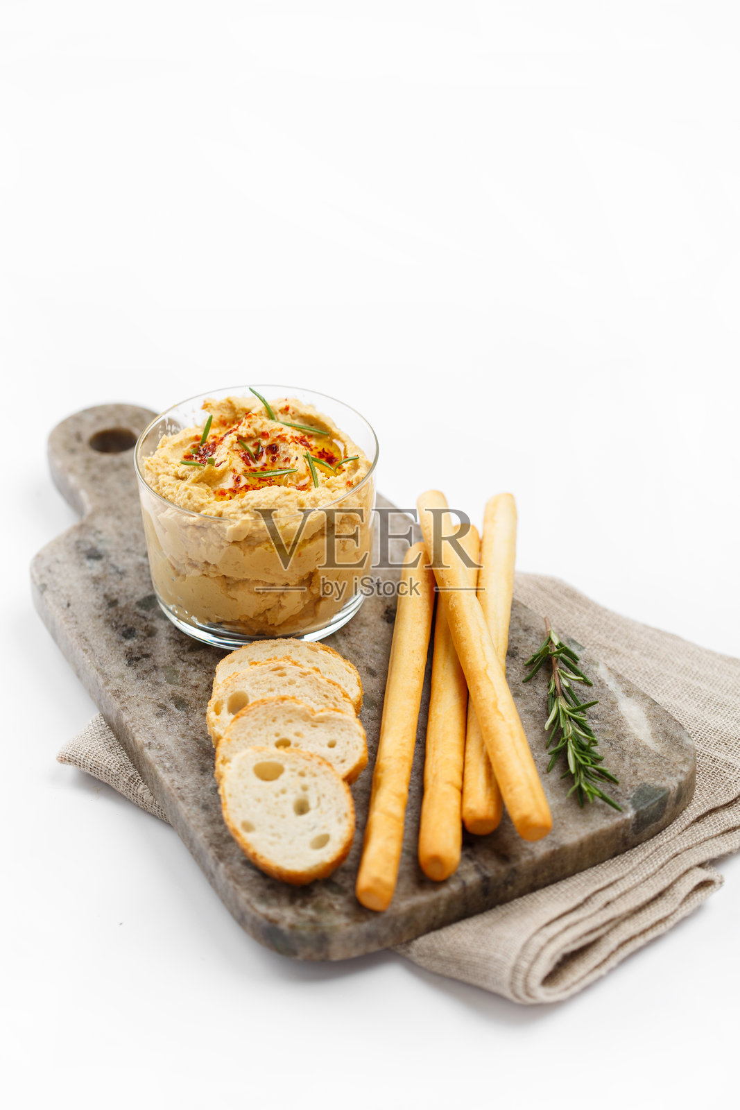 玻璃杯中的鹰嘴豆泥，配以迷迭香和红辣椒片，旁边放着面包，摆放在大理石切菜板上照片摄影图片