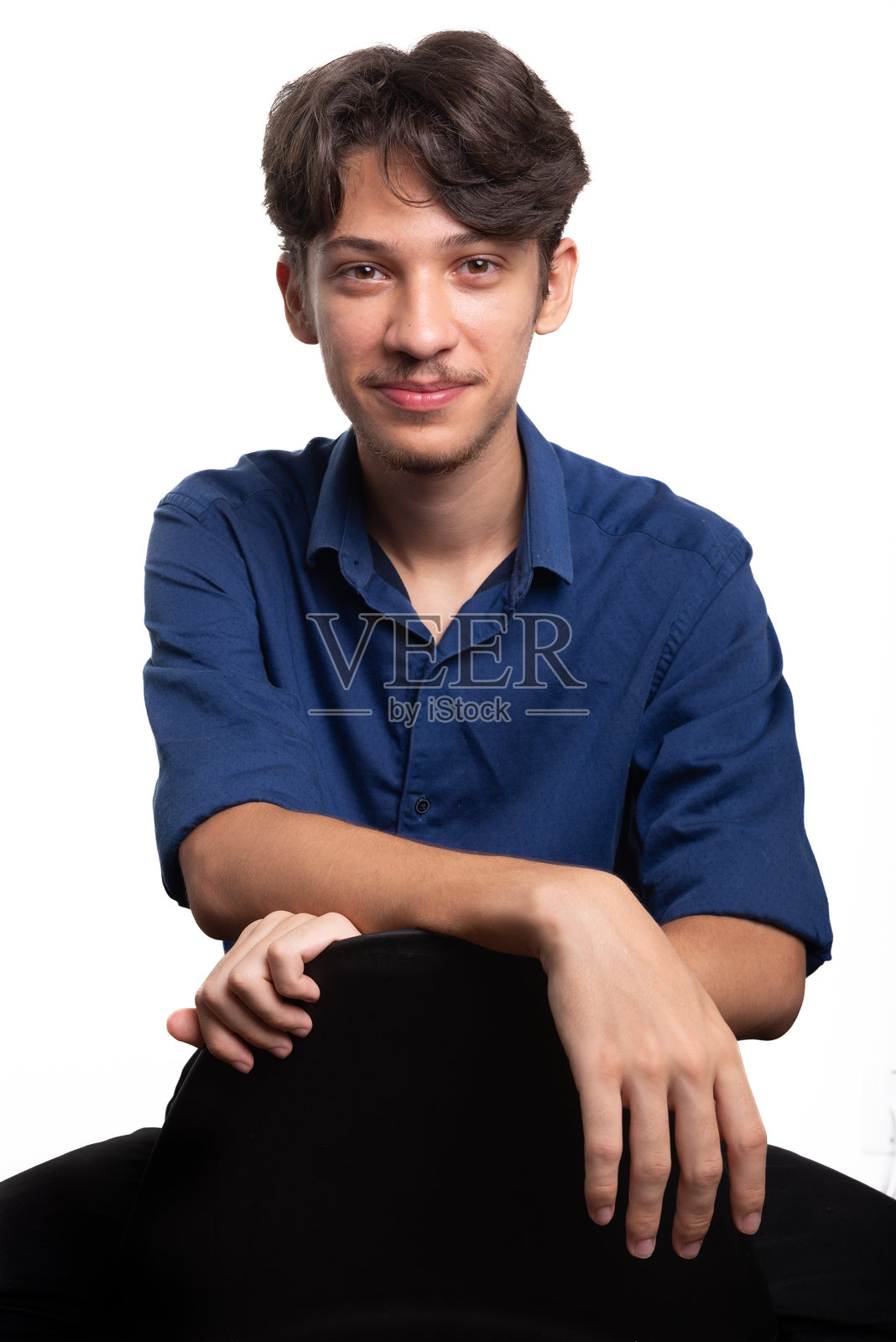 年轻帅气的学生，黑发蓝衬衫，坐着微笑，注视着镜头。背景为白色。自信的人。照片摄影图片
