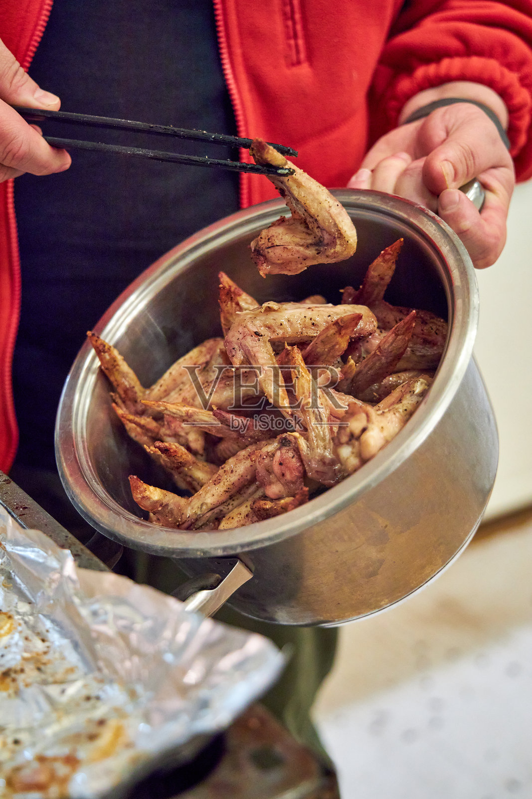 一个男人把烤箱烹饪的鸡翅放进锅里照片摄影图片