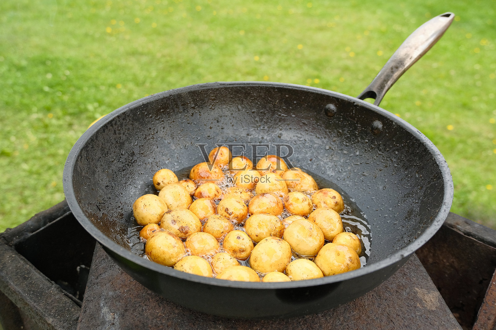 在热油中用黑色铁锅炸的小土豆。照片摄影图片