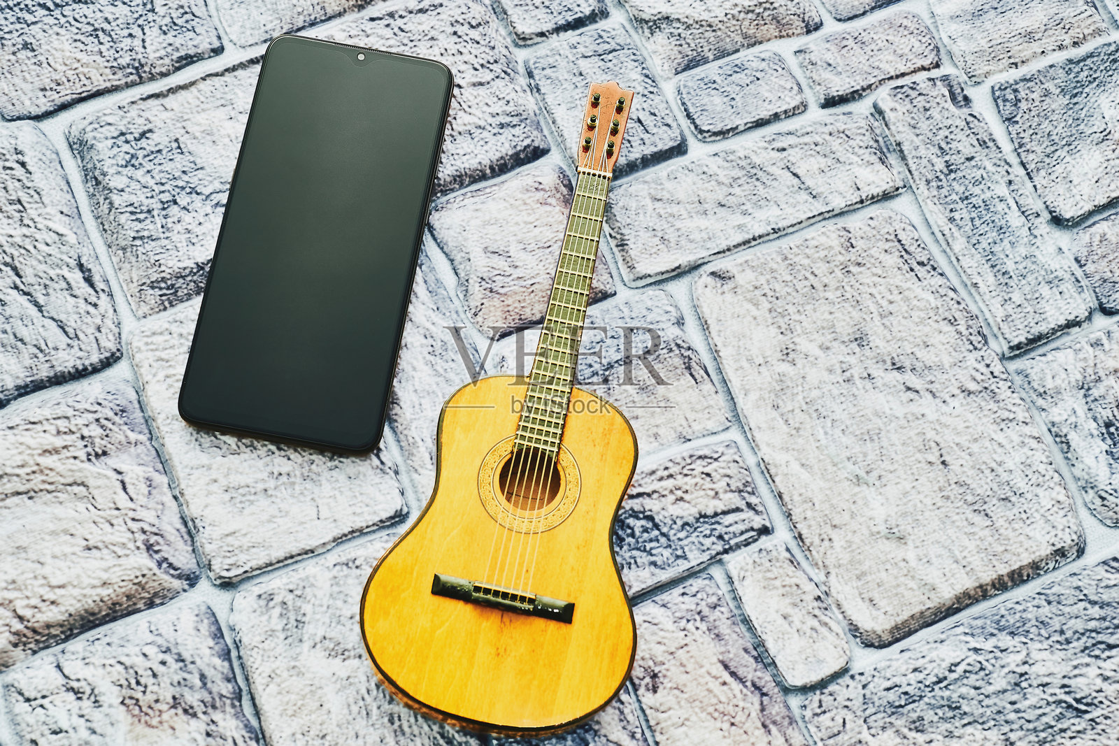 黄色的木吉他，带有文本空间的手机，背景为鹅卵石铺成。照片摄影图片