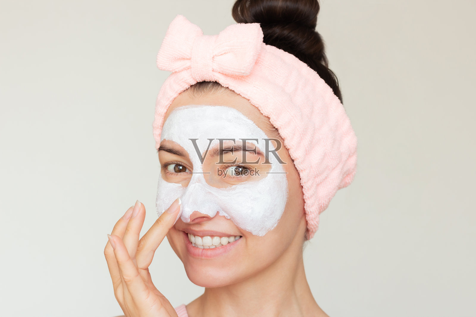 年轻漂亮的女人戴着粉色头带，脸上带着白色口罩，正对着镜头微笑并享受自己。照片摄影图片